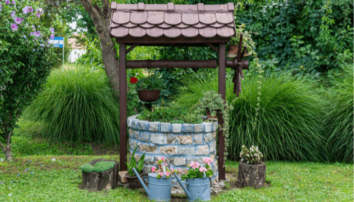 Decorative stone water well surrounded by summer greenery and flowers in Western NY