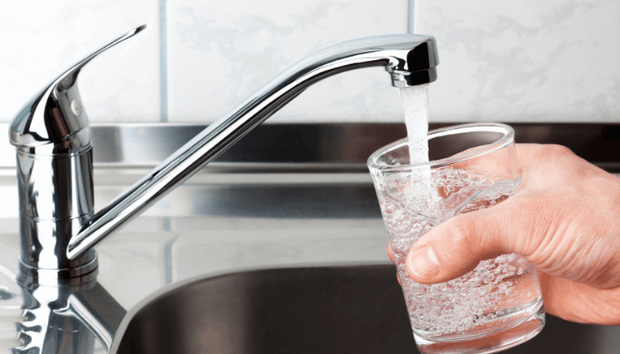 Hand filling a glass of tap water in a kitchen sink, representing clean drinking water and home water testing in Western New York.